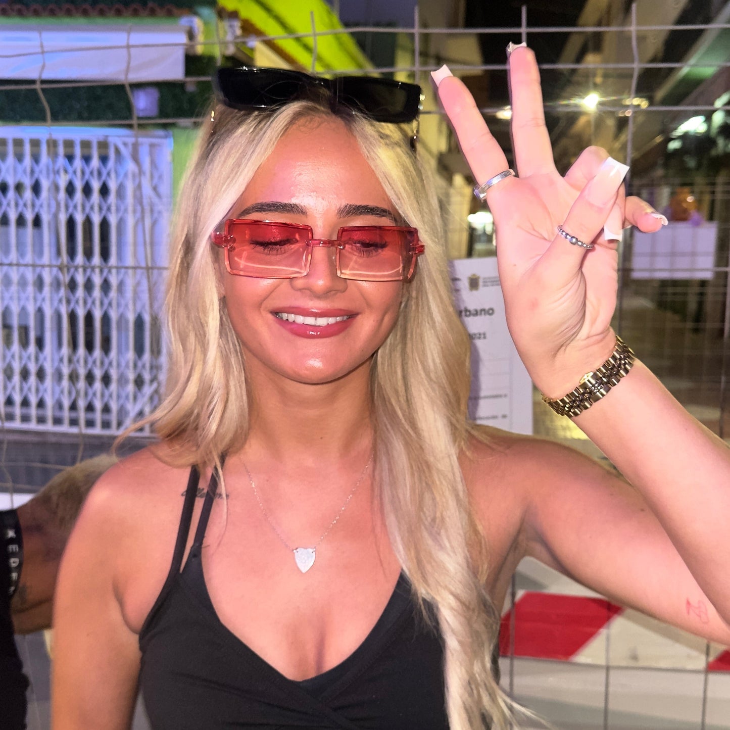 Woman wearing sunglasses and a black top, making a peace sign.